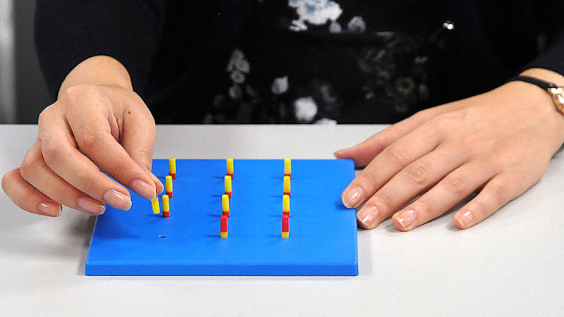 A person sat at a desk with red and yellow pegs in a blue peg board